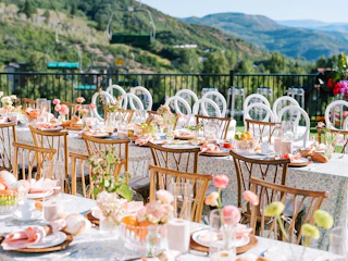 Outdoor tablescape at Viceroy Snowmass on the Lift Line Deck with two long tables, wooden chairs, florals, plates, and napkins in the foreground and a lift line in the background on a sunny day.